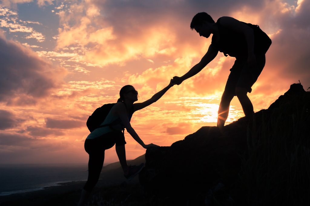Team work. Man and woman helping each other climb up a mountain.